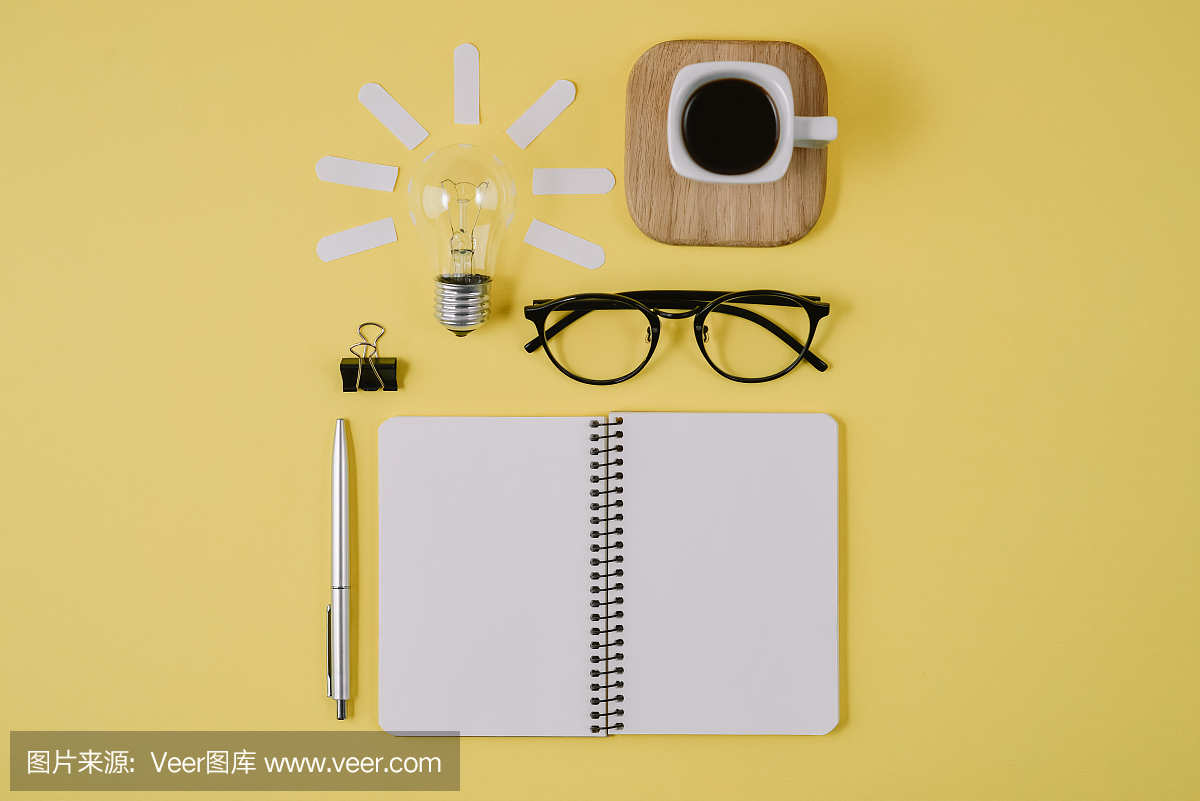 创意平铺概念顶视图的工作桌风格的设计办公用品与笔,记事本,眼镜,杯咖啡和灯泡在黄色的背景。概念的头脑风暴